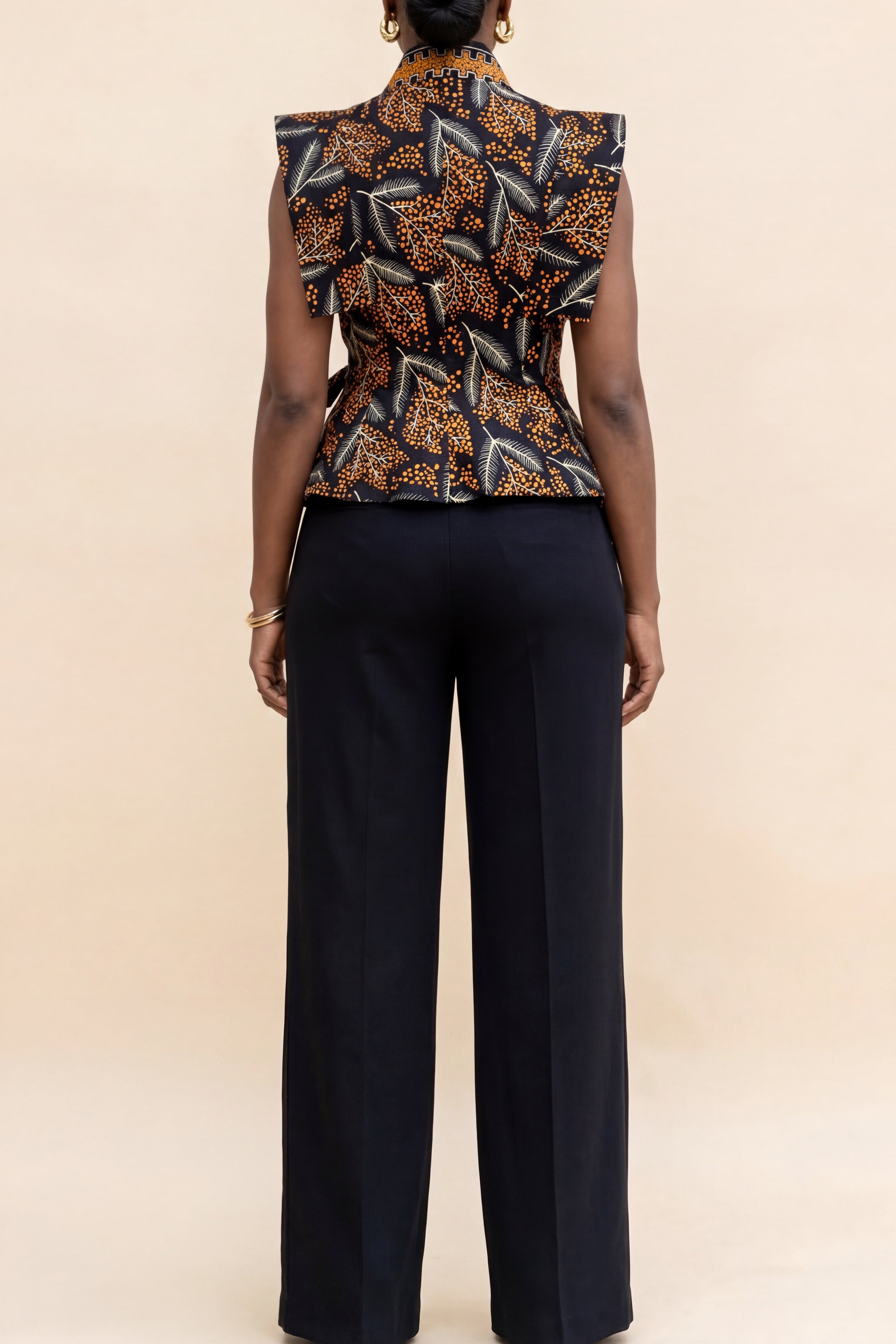 Person wearing a patterned top and black pants on a beige background