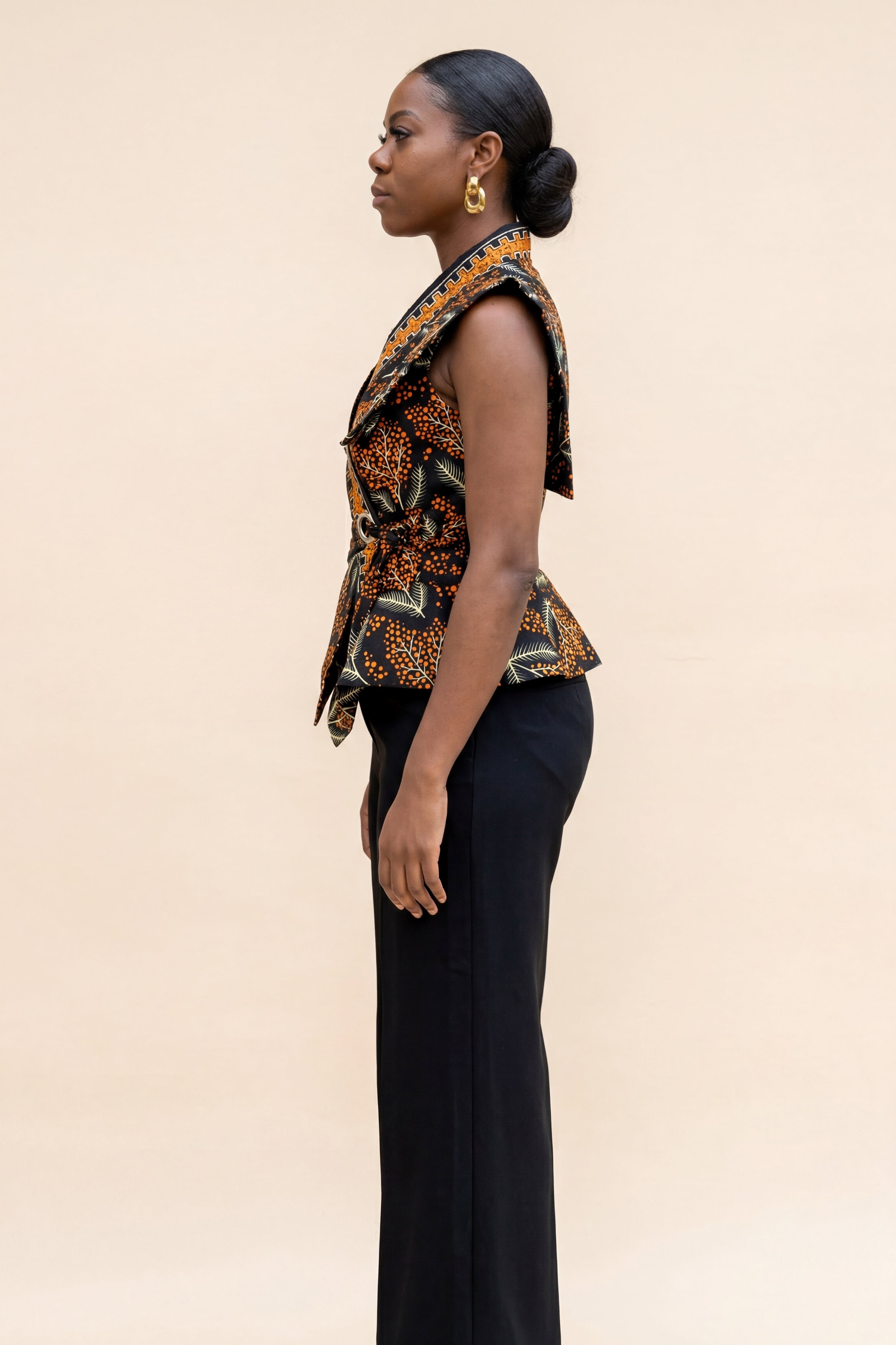 Woman wearing a patterned top and black pants on a beige background
