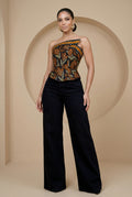 Woman wearing a strapless top with a pattern and black pants against a beige background